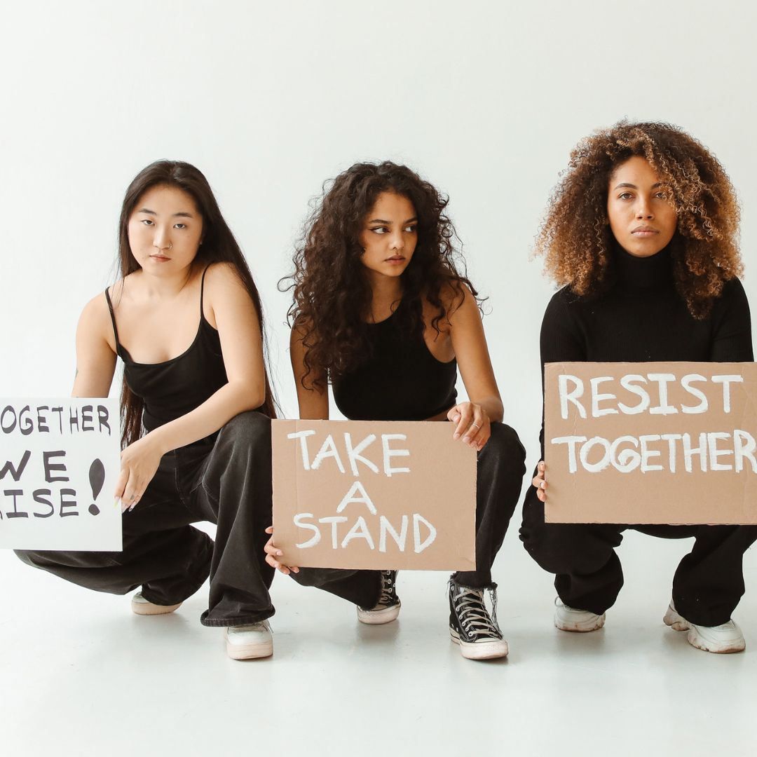 Women holding signs that say together we rise, take a stand, resist together